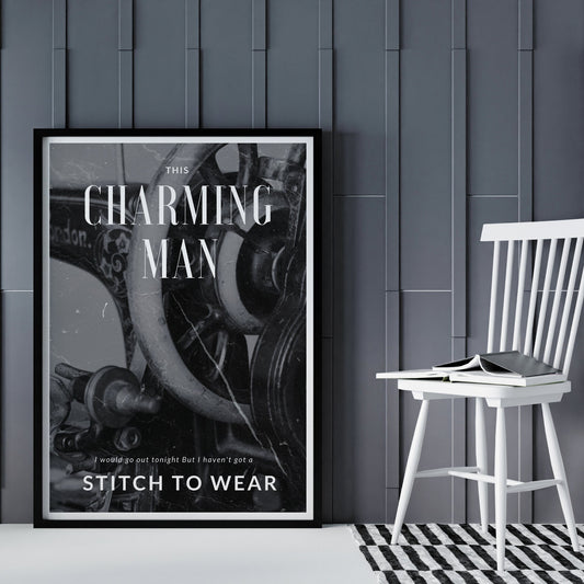 A black and white poster featuring the text 'Charming Man' and a graphic of a sewing machine, displayed on a wall above a white chair with a book on it, set against a background of gray wooden panels.