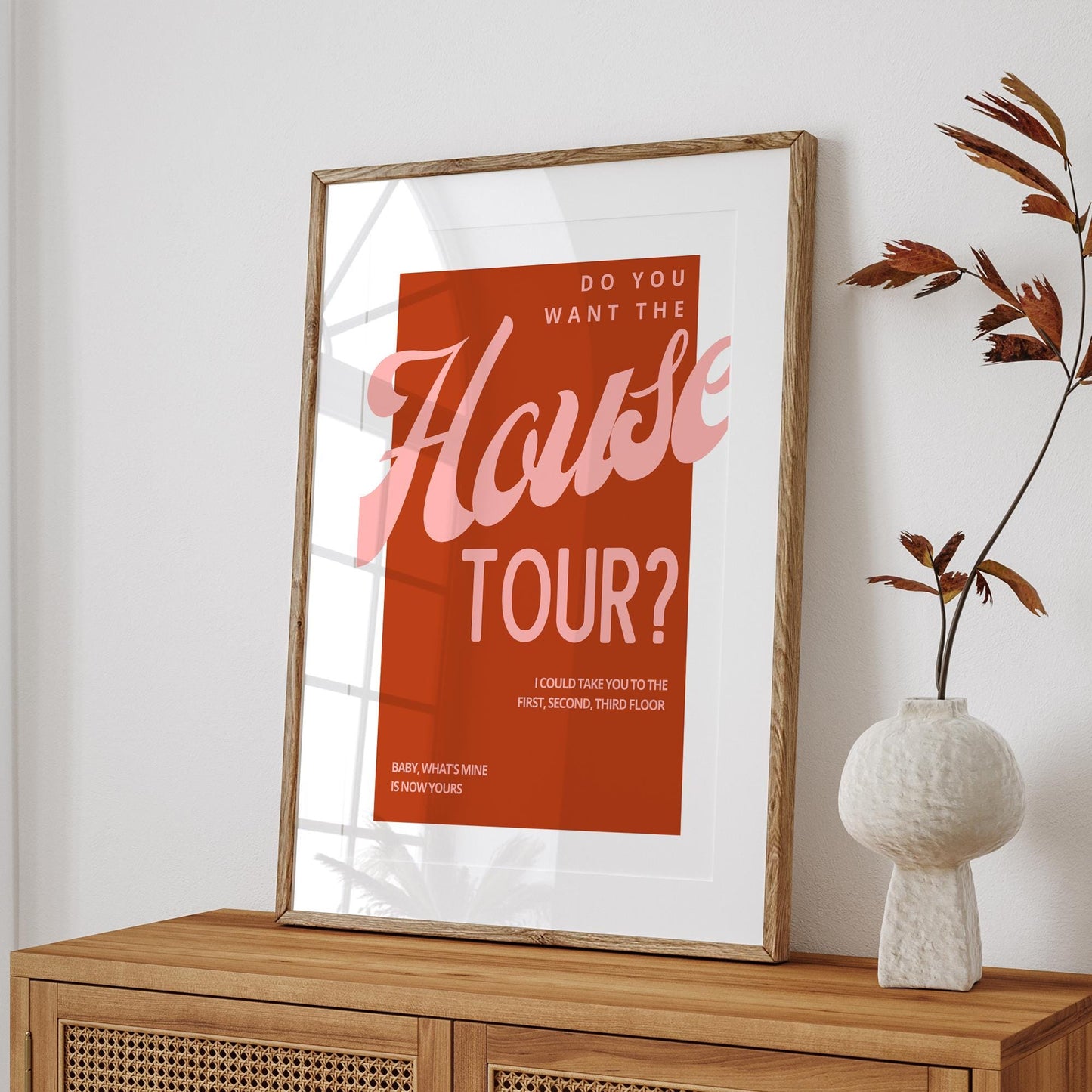 Framed poster with 'Do you want the house tour?' text on a wooden shelf with a vase.